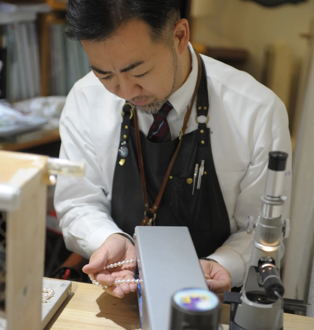 真珠ネックレスを手に持ち、専用の機械で磨く作業