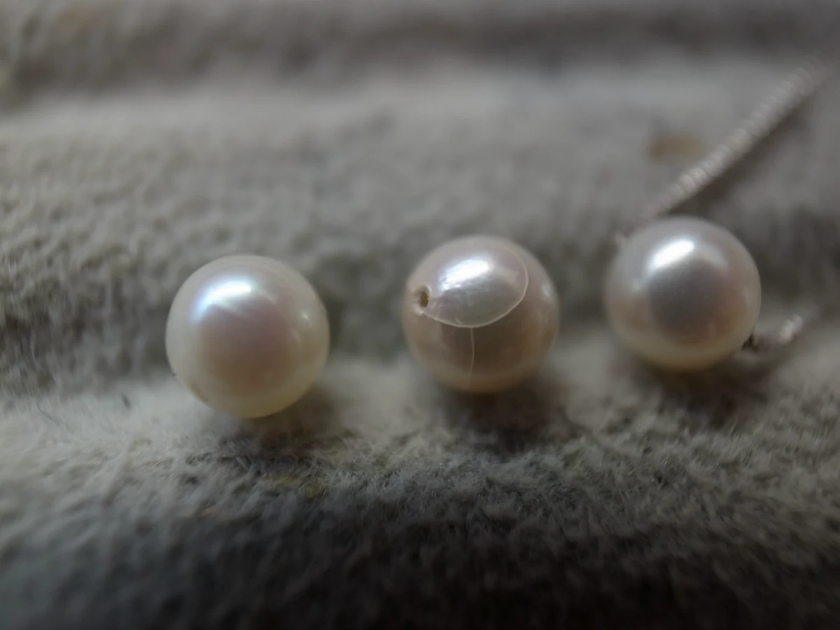 布の上の三つの真珠とピアス部品。珠の形や穴の位置を観察する加工例