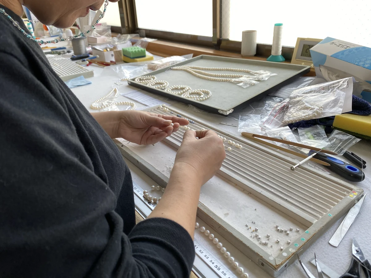 加工現場で、溝のある台に真珠を並べて選別する手元